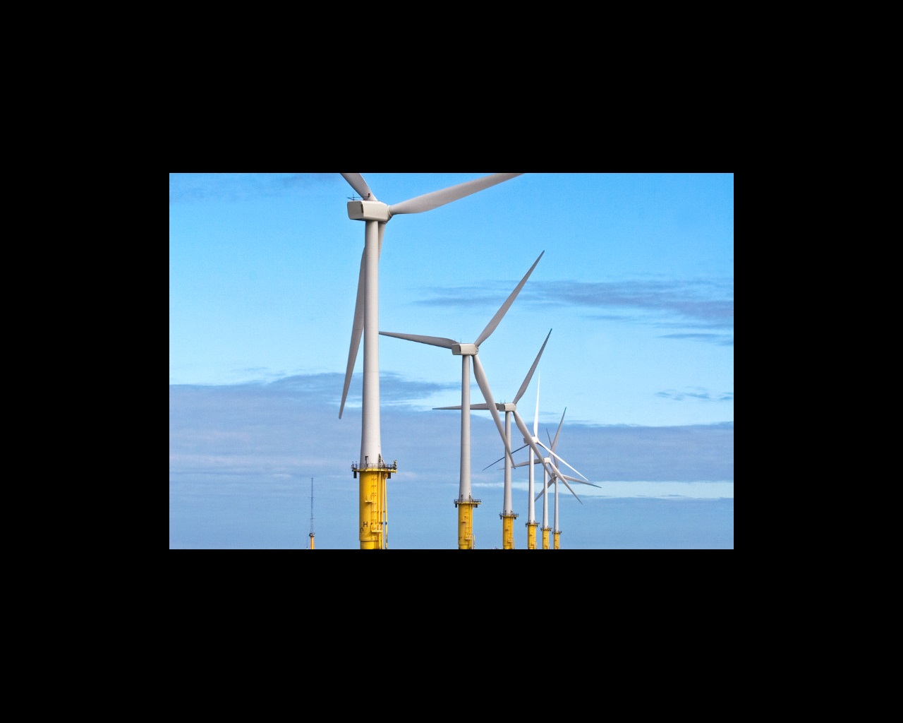 A row of tall wind turbines on yellow bases against a blue sky with clouds.