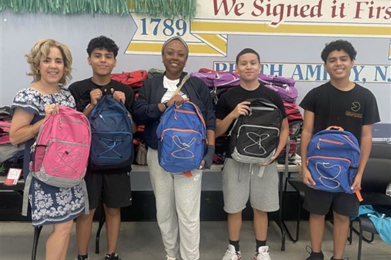 A group of five individuals, including one adult, holding colourful backpacks in a setting filled with more backpacks.
